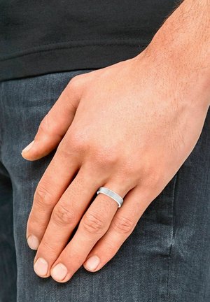 A close-up of a hand resting on dark jeans, showcasing a simple silver ring on the ring finger. Skin tone is light, with visible fingernails.