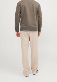 Sudadera de color verde oliva con puños y dobladillo acanalados, combinada con pantalones holgados de color beige claro y zapatillas negras y blancas.