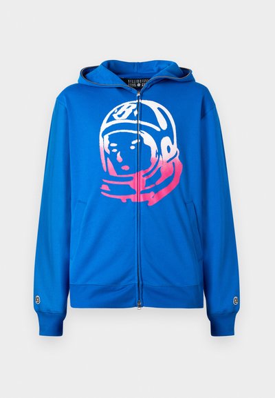 Modra zip-up kapuca z roza in belo grafiko astronavta spredaj. Narejena iz mehkega materiala, z stranskimi žepi in rebrastimi manšeti.