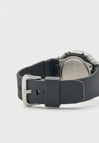 Μαύρο λουράκι ρολογιού από λάστιχο με υφή, ασημένια μεταλλική αγκράφα. Ανοικτή πίσω πλευρά από ανοξείδωτο ατσάλι με χαραγμένες λεπτομέρειες.