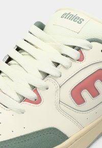 Άσπρο δερμάτινο αθλητικό παπούτσι με λεπτομέρειες σε μέντα πράσινο, ροζ λογότυπο και υφασμένα λευκά κορδόνια. Διαθέτει λείο φινίρισμα και εμφανείς ραφές.