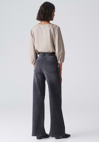 Weite, dunkelgraue Jeans mit Gesäßtaschen, kombiniert mit einer beigen, strukturierten Bluse mit viereckigem Ausschnitt und Puffärmeln.