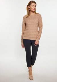 Pulover texturat bej cu modele orizontale, purtat cu pantaloni negri ajustați și mocasini bej. Puloverul are mâneci lungi și decolteu rotund.