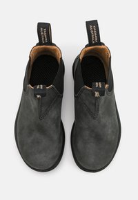 Botas de tobillo de cuero negro con paneles laterales elásticos, punta redonda y suelas con textura. Presentan un lazo en la parte posterior etiquetado "Tasmania Australia".