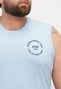Chemise sans manches en coton bleu clair arborant un logo circulaire noir avec le texte "JACK & JONES 1990 COLLECTORS CREW" sur le devant.
