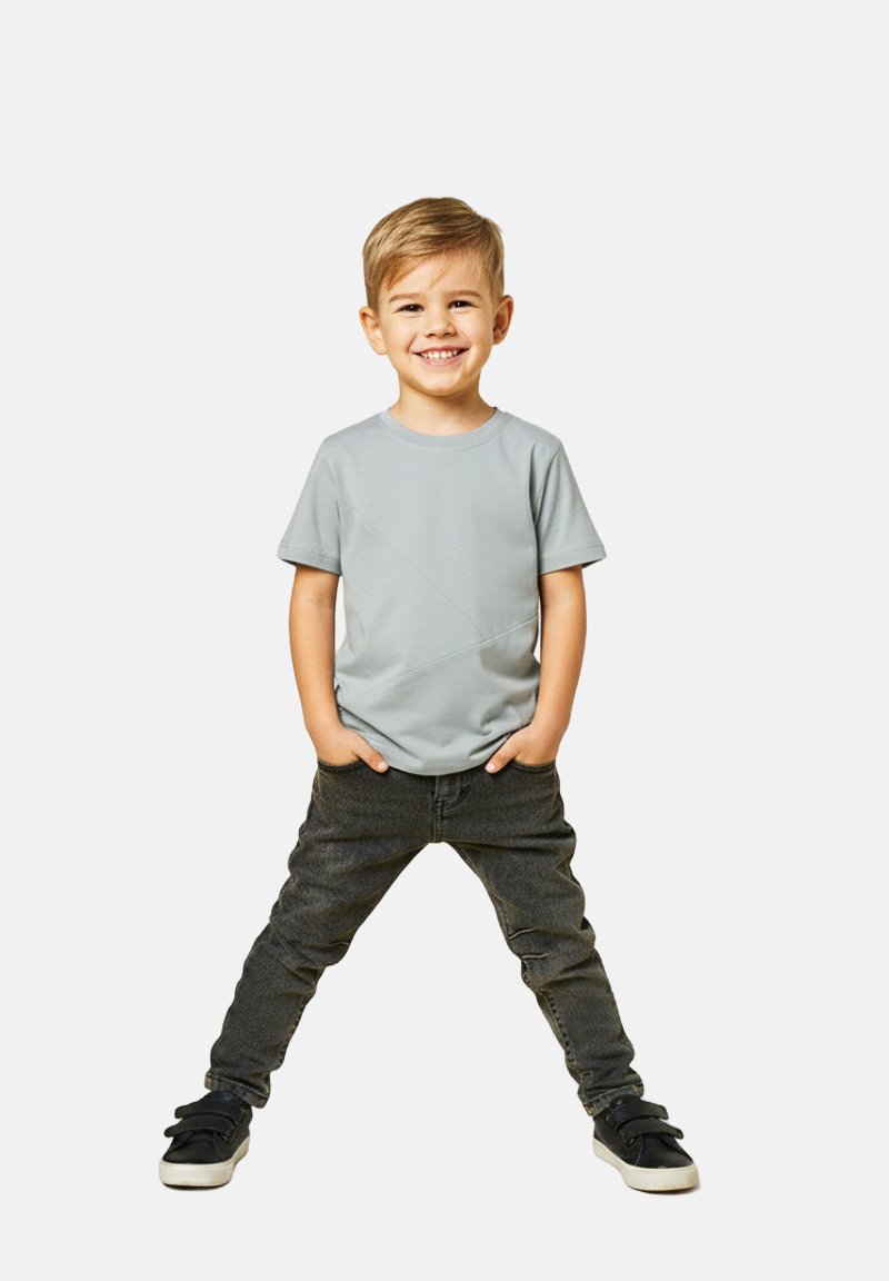 Szara koszulka z krótkim rękawem z ukośnym wzorem przeszyć, zestawiona z ciemnymi dżinsami i czarnymi trampkami z paskiem na rzep. Dziecko stoi z rękami w kieszeniach.