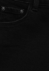Gros plan sur un tissu en denim noir montrant une poche avant avec des rivets métalliques et des coutures visibles.
