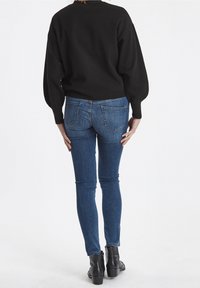 Sudadera negra de punto con mangas abullonadas combinada con jeans ajustados azules y botas negras de tobillo. El conjunto destaca un estilo casual y cómodo.