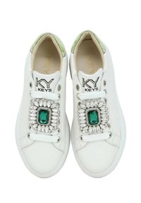Sneakers bianchi con un accento verde sul tallone, impreziositi da un grande gemma verde e cristalli di strass argentati sui lacci.