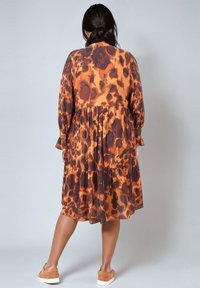 Robe à imprimé léopard brun et orange avec des manches longues, une jupe à volants et une coupe ample, associée à des chaussures en daim brun.