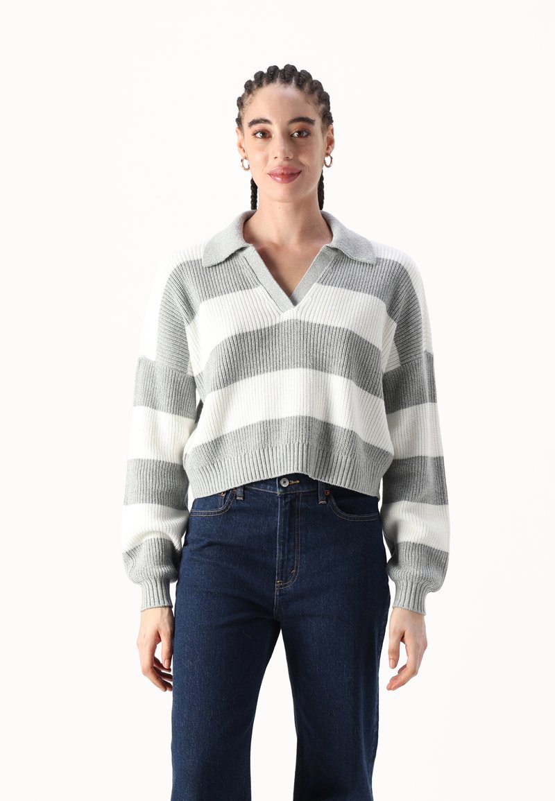 Szary i biały, w paski, krótki sweter z dekoltem w serek i kołnierzykiem. Dzianinowa tekstura i ściągacze na rękawach. Zestawiony z ciemnymi dżinsami z wysokim stanem.