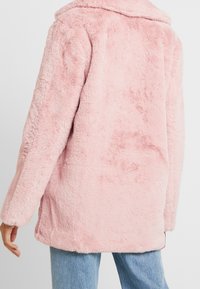 Rosa Mantel aus Kunstfell mit weicher Textur, langen Ärmeln und einem Kragen. Hat einen geraden Schnitt und minimalistische Details auf der Rückseite.