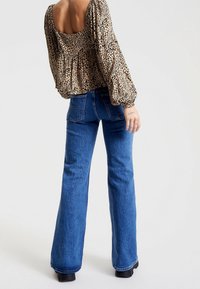 Blusa a stampa animale con maniche a sbuffo e schiena quadrata, abbinata a jeans in denim blu a zampa d'elefante con tasche posteriori e vestibilità casual.