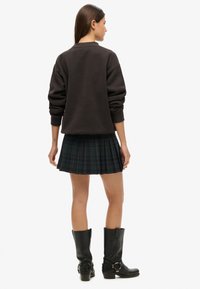 Sort bomulds sweatshirt med dropped shoulders, parret med en plisseret grøn tartan nederdel. Iført knæhøje sorte læderstøvler.
