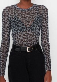 Top a maniche lunghe in tessuto trasparente con motivo leopardato grigio e nero, abbinato a jeans neri a vita alta e una cintura nera.