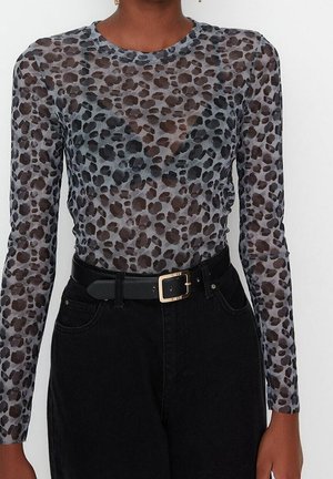 Langærmet, gennemsigtig bluse med et grå og sort leopardmønster, parret med højtaljede sorte jeans og et sort bælte.