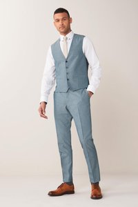 Hellblauer, maßgeschneiderter Weste mit passender Hose, aus strukturiertem Material. Weißes Hemd mit spitzem Kragen und einer gemusterten Krawatte. Braune Lederschuhe.