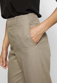 Beige corduroy pants featuring a tailored fit, side pockets, and a smooth texture. The waistband is finished with subtle stitching details.