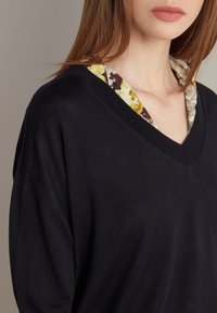Černý svetr s výstřihem do V, s květinovým vzorem, který se rýsuje z límce. Měkká textura a volný střih.