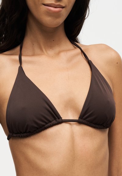 Femme portant un haut de bikini triangulaire marron foncé avec de fines bretelles nouées derrière le cou, souriant légèrement.