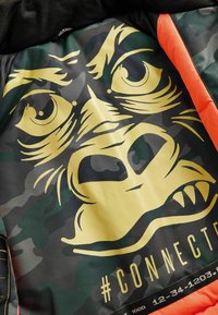 Padded jacket interior featuring a large gorilla face graphic in yellow on a green camo background. Black and orange accents at the edges.