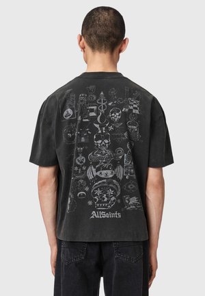 Άτομο που φοράει μαύρο t-shirt με λευκές περίτεχνες εικονογραφήσεις που περιλαμβάνουν κρανία, φίδια, αστέρια και το κείμενο "AllSaints" στην πλάτη.