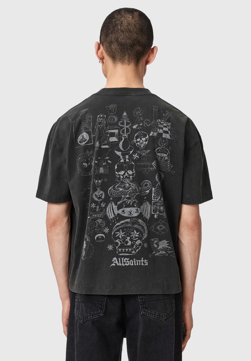 Άτομο που φοράει μαύρο t-shirt με λευκές περίτεχνες εικονογραφήσεις που περιλαμβάνουν κρανία, φίδια, αστέρια και το κείμενο "AllSaints" στην πλάτη.