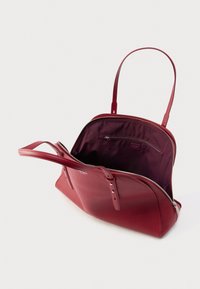 Sarkana ādas soma ar strukturētu formu, dubultiem rokturiem, augšējo rāvējslēdzēju un dziļu tumši sarkanu interjeru ar rāvējslēdzēja kabatu.