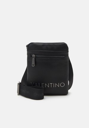 Sac bandoulière noir Valentino avec poche zippée à l'avant, sangle réglable en tissu et lettrage logo argenté sur surface en cuir lisse.