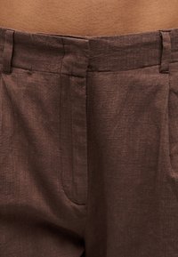 Κοντινό πλάνο στη μέση και το φερμουάρ καφέ λινών παντελονιών που φορά ένα άτομο με ορατό δέρμα πάνω από τη γραμμή μέσης.