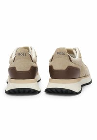 Sneakers in suede beige e rete, con dettagli in pelle marrone. Presentano una suola intermedia bianca e una suola esterna in gomma nera. Logo mostrato sul retro.