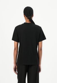 Svart t-shirt med rund hals i bomull, med korta ärmar och en avslappnad passform. Baksidan har en ren, sömlös design.