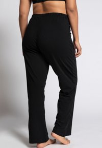 Schwarze, elastische Bundhose mit lockerer Passform und geraden Beinen; aus weich gewebtem Stoff mit minimalen Nähten und ohne auffällige Muster.