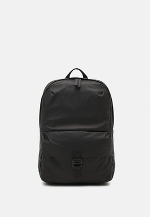 Mochila negra hecha de un tejido suave con forma rectangular, que cuenta con un cierre frontal y un asa en la parte superior para transportar.