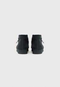 Black suede ankle boots with a round toe, featuring stitching details and a solid rubber sole. Laces are tied at the back.
