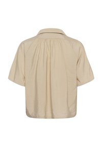 Blouse beige à manches courtes avec des détails froncés sous le col arrière et une coupe ample.