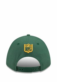 Casquette de baseball verte avec une fermeture à clip réglable. Présente un patch du logo NFL jaune et des coutures à l'arrière. Fabriquée en tissu avec une texture lisse.