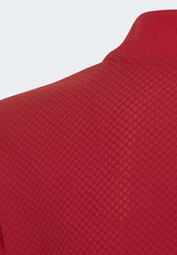 Polo shirt rouge avec un motif en losanges texturé, doté d'un col classique et de manches courtes. Le matériau semble léger et respirant.