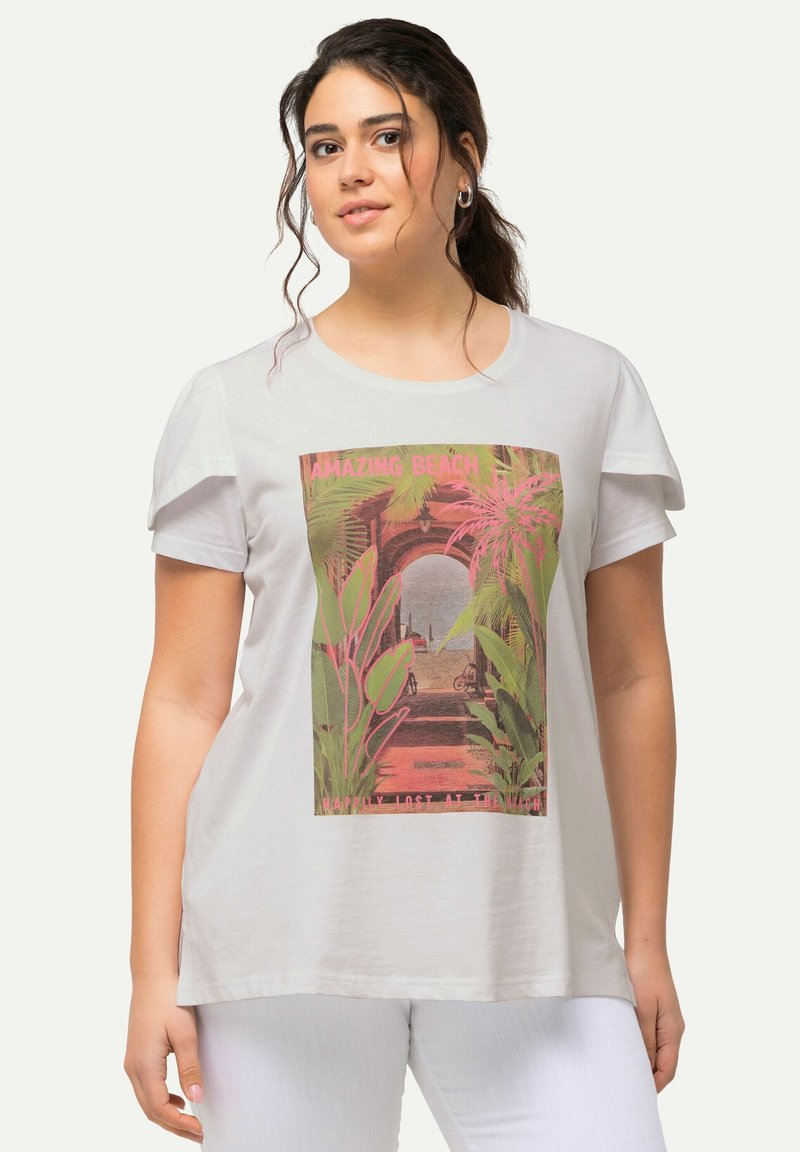 Camiseta blanca de corte relajado con un gráfico colorido de "Playa Increíble" que presenta hojas de palma y una escena de playa. Mangas cortas con textura suave.