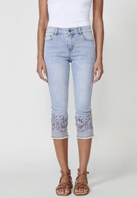 Light blue denim capri jeans with intricate embroidered hem. Features a fitted design, five pockets, and a button fly closure.