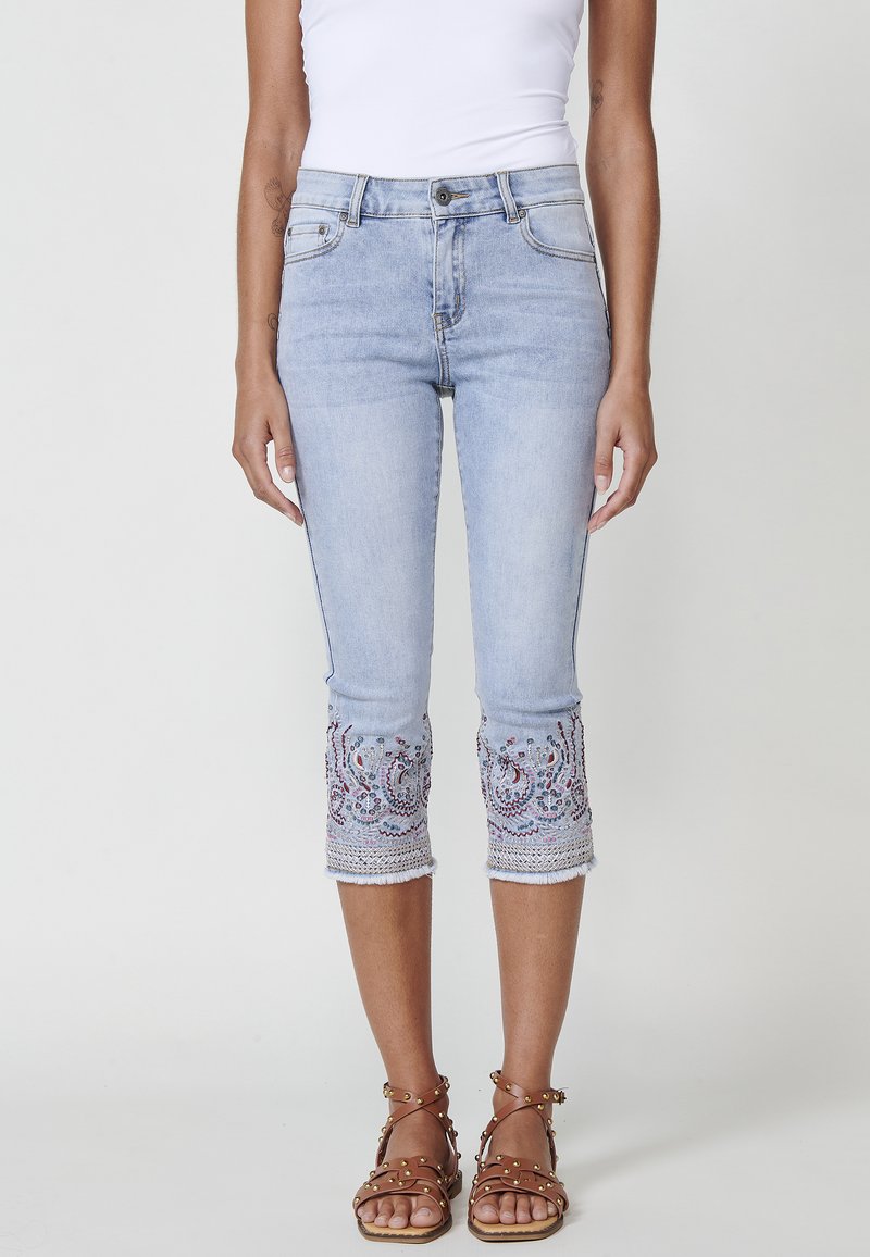 Light blue denim capri jeans with intricate embroidered hem. Features a fitted design, five pockets, and a button fly closure.