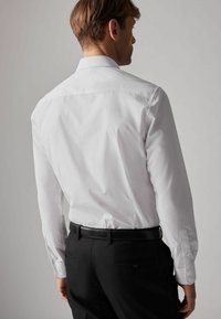Weißes Langarmhemd mit Button-Down-Kragen, kombiniert mit schwarzen Hosen. Hat glattes Material und sichtbare Nähttdetails.
