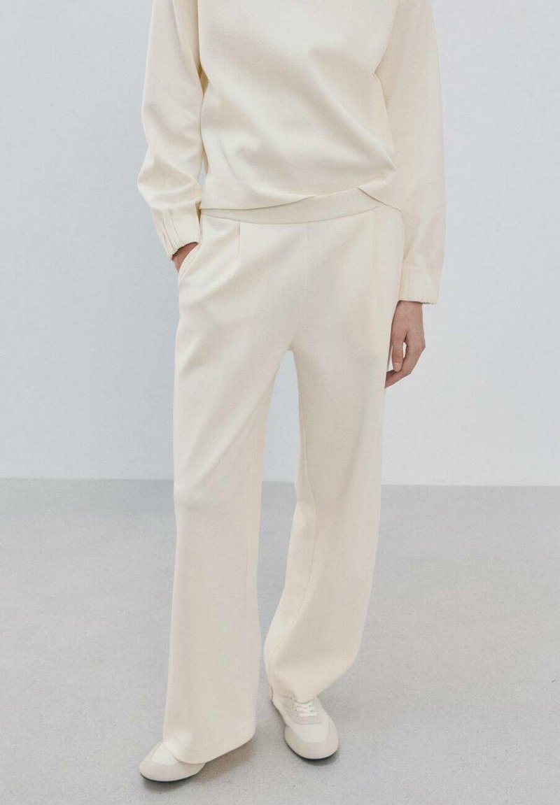 Komplet za opuštanje u boji kreme koji se sastoji od dugih rukava i širokih hlača, izrađen od mekanog materijala s glatkom teksturom i džepovima.