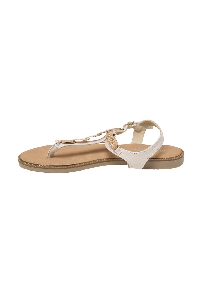 Beige flad sandal med T-rem, ankelrem og dekorative ovale metal accenter på en brun polstret sål.