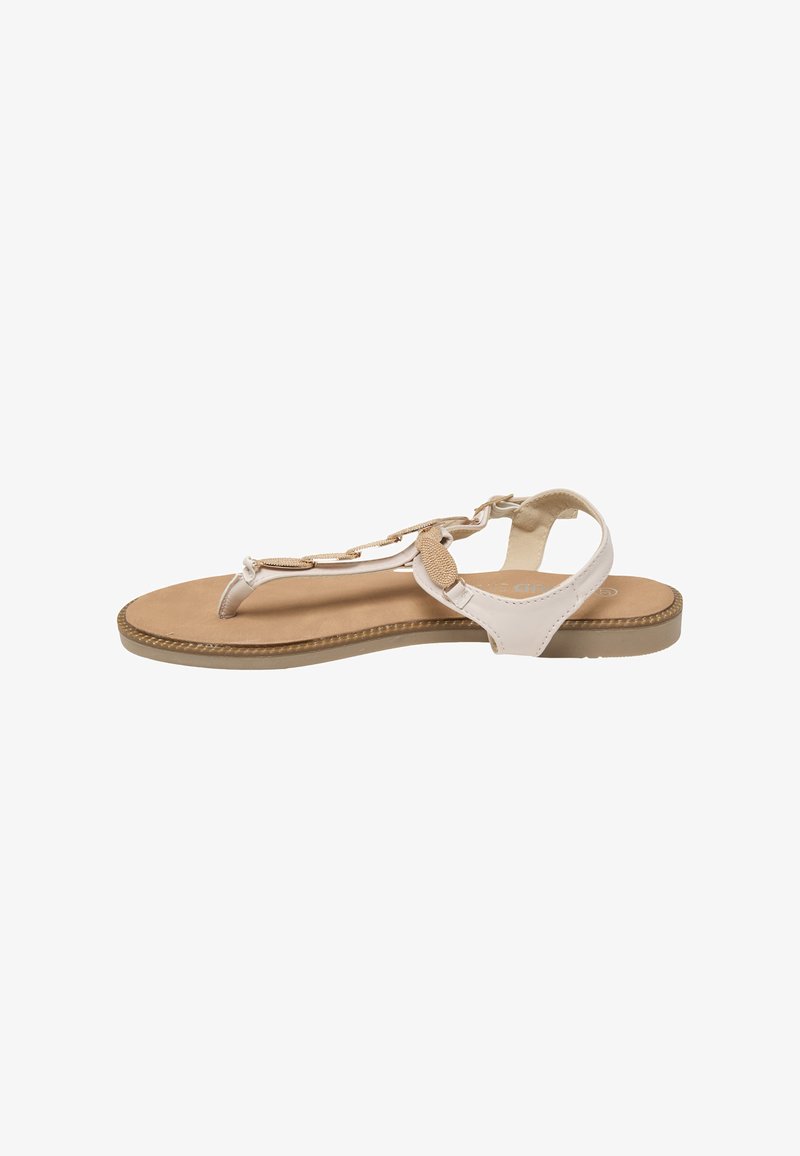 Beige flad sandal med T-rem, ankelrem og dekorative ovale metal accenter på en brun polstret sål.