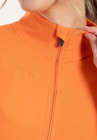 Zip-up jacka i livfullt orange tyg med hög krage och svart dragkedja. Har sömlös design och lätt glans för en modern look.