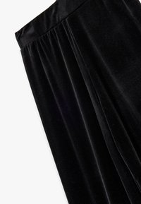 Sort fløjlsnederdel med en glat tekstur, skræddersyede plisseringer og et bredt linning. Stoffet reflekterer lyset diskret.