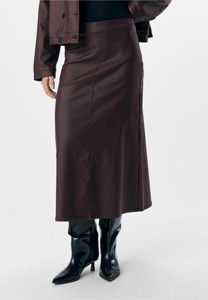 Jupe midi en cuir marron foncé associée à une veste assortie et des bottines noires brillantes à talons hauts à bout pointu.