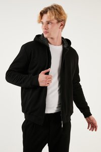 Čierna mikina na zips s textúrovaným sivým interiérom, dlhými rukávmi a elastickými manžetami, nosená cez biele tričko, vystavená na svetlom pozadí.