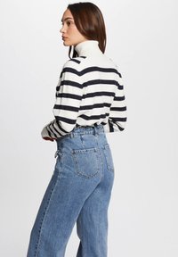 Pull à col roulé rayé en blanc et marine, avec une texture côtelée ; associé à un jean en denim bleu taille haute avec poches.